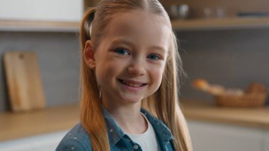 Sevimli, beyaz, kız çocuğu, dişlek, gülümseyen, ev mutfağında çekilmiş bir fotoğrafa bakan, çocuk bakımı, velayet hekimliği, çocuk sağlığı ve çocuk sağlığı kavramını benimseyen çocuk.