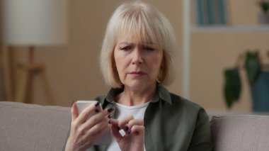 Cep telefonlu yaşlı beyaz kadın üzgün üzgün üzgün üzgün üzgün evde kameraya bakıyor yaşlı bayan büyükanne kötü haber reddetme olumsuz bağlantı hatası hissediyor