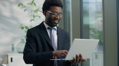 Ofiste dizüstü bilgisayarı yazan düşünceli Afro-Amerikalı işadamı pencereye bakıyor düşünceli, odaklanmış, etnik iş adamı profesyonel bilgisayar, internet, şirket ajanı.
