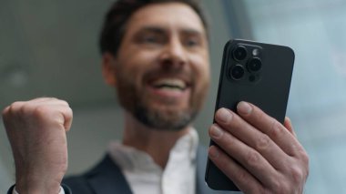 Beyaz erkek işadamı, başarıyı akıllı telefonla kutlamaktan heyecan duyuyor. İyi haberler alıyor, cep telefonu mesajları alıyor. Finansal iş başarısı. Çevrimiçi kazanma başarısı.