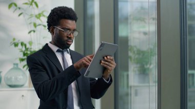 Odaklanmış Afro-Amerikan işadamı dijital tablet kullanarak internet üzerinde çalışan kablosuz bilgisayar teknolojisi iş adamı erkek işvereni ile veri analizi yapıyor.