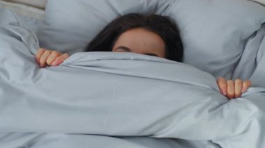 Kafkasyalı gülümseyen kadın battaniyenin altına saklanmış kameraya bakıyor gülüşü dişlek, neşeli, kaygısız gülüşü sabah yatak odasında gizlice gözetleyerek uyanan kız.