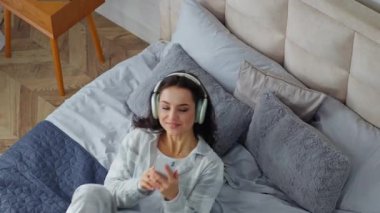 Kafkasyalı bir kadın rahat yatağın üzerine düşüyor. Yatak odasında gülümseyen bir kız. Sohbet eden cep telefonu uygulaması kullanıyor.