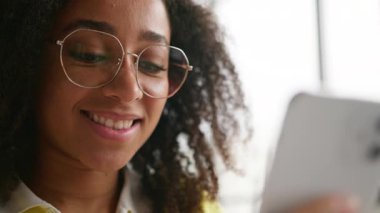 Üniversitede cep telefonuyla gezmekten hoşlanan Afro-Amerikalı bir kadın okul akademisinde sosyal medyada komik videolar izleyen akıllı telefon teknolojisiyle memnun bir kız öğrenci.