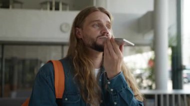 Olumlu konuşan Kafkasyalı erkek öğrenci modern cep telefonu teknolojisiyle sesli mesaj kaydediyor. Akıllı telefon kullanımı internet asistanı uygulaması ile konuşup üniversitede sesli mesaj gönderiyor.