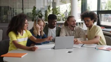 Beş farklı etnik çeşitlilikte öğrencilerden oluşan bir ekip dizüstü bilgisayarla gülerek eğleniyor, internette ev ödevlerini tartışıyor e-öğreniyor, komik sohbetler yapıyor üniversitede bilgisayar konuşmalarına gülüyor.