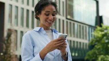 İnanılmaz gülümseyen Afro-Amerikan iş kadını akıllı telefon şebekesi yazan açık hava bayan girişimci iş kadını iyi haber cep telefonu mesajı alıyor çevrimiçi başarı tepkisi kentsel teknoloji kazandı