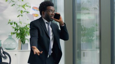 Öfkeli Afrikalı Amerikalı işadamı cep telefonuyla bağırıyor modern ofis işadamı hayal kırıklığına uğramış evrakları fırlatıyor pencereden dışarı bakıyor erkek yönetici stresli çatışma çağrısını bastırıyor