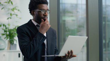 Ofiste dizüstü bilgisayarı yazan düşünceli Afro-Amerikalı işadamı pencereye bakıyor düşünceli, odaklanmış, etnik iş adamı profesyonel bilgisayar, internet, şirket ajanı.
