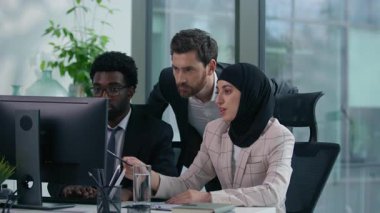 Modern ofisteki çok kültürlü iş arkadaşları tesettürde çalışan Afrika kökenli Amerikalı erkek kadın ve beyaz adam bilgisayar karşısında takım çalışması üzerine tartışıyorlar.