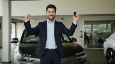 Araba anahtarlarını tutan mutlu Kafkasyalı iş adamı otomobil piyangosunu kazandı. Erkek alıcı yeni otomobil alımını kutluyor. Gülümseyen sahibi, kredi hizmeti nakliye galerisini sevindirdi.