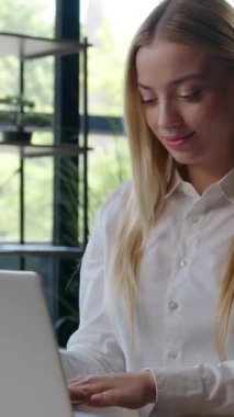 Masada dizüstü bilgisayarı yazan beyaz bir iş kadını kameraya gülümseyen mutlu Avrupalı iş kadını iş kadını kız işveren. İnternet projesiyle çalışıyor. Ofisteki bilgisayardan e-postaları kontrol ediyor.