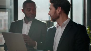 İki çok ırklı iş adamı ve dizüstü bilgisayar ortaklığı işadamları ofiste birlikte çalışıyorlar. Kafkasyalı bir adam Afrikalı Amerikalı erkek iş arkadaşlarıyla konuşuyor. Satışlar mutlu başlangıç fikri üzerinde görüşüyorlar.