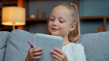 Kafkas kız çocuğu kız çocuğu defter içinde ders okuyor evde uzaktan eğitim okuyor ilkokul öğrencisi, ev ödevi notları hazırlıyor oturma odasında öğreniyor