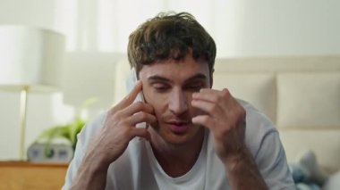 Neşeli, gülümseyen, beyaz bir genç adam yatak odasında akıllı telefonuyla konuşuyor. Mutlu Avrupalı iş adamı gülen cep telefonuyla konuşuyor.