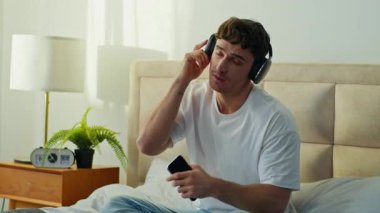 Aktif Kafkasyalı adam yatak odasında uzanıyor kulaklık takıyor müzik dinliyor erkek sesli eğleniyor alet kulaklıkları kullanıyor evde kablosuz çalma listesi teknolojisi gevşemesi kullanıyor