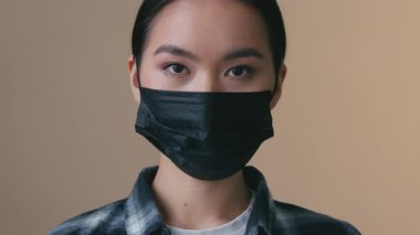 Ciddi bir Asyalı kadın, siyah tıbbi maske takıyor. Kamera görüntüsü var. Kordemik koronavirüs enfeksiyonu var.
