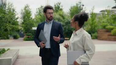 Çok ırklı iş arkadaşları, Afrika kökenli Amerikalı kadınla sohbet ediyor. Beyaz adam şehirde yürüyor. Elinde dizüstü bilgisayarla geziyor.