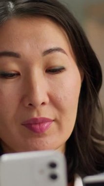 Orta yaşlı Asyalı kadın, elinde cep telefonu olan, Koreli iş kadını akıllı telefon Japon ofis kadınıyla banka ödemesi almaktan mutlu bir şekilde internetten alışveriş yapıyor.