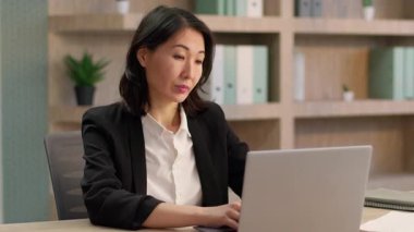 Yetişkin Çinli iş kadını Koreli bayan Asyalı iş kadını kameraya bakıyor gülümsüyor orta yaşlı ofis çalışanı bilgisayar işçisi yetişkin girişimci kadın çevrimiçi gülümsüyor.