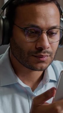 Sakin Hintli Arap iş adamı ofis masasında kulaklıkla müzik dinliyor. Cep telefonu erkek işadamı ses uygulamasında şarkı seçiyor. Dinlenme molası veriyor.