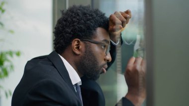 Acı çeken Afrikalı Amerikalı iş adamı erkek işadamı aşırı çalışma panik atağını vurguladı. Ofis camına yaslandı. İflas sorunu, işten çıkarma, işsizlik, stres, iş başarısızlığı.