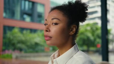 Afrika kökenli Amerikalı iş kadını yüzünü çevirerek kameraya bakıyor. Ciddi iş kadını, etnik kız girişimci, şehir merkezinde ofis dışında poz veren baş kadın.