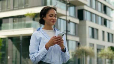 Gülümseyen mutlu Afro-Amerikan iş kadını şehirde akıllı telefon tutuyor neşeli kadın girişimci ofis kadını hayali kuruyor internetten sohbet eden internet teknolojisini kaçırmayı düşün.