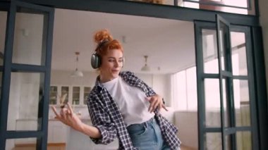 Mutlu beyaz kadın yeni kablosuz kulaklıklarla dans ediyor neşeli kadın kulaklıklarıyla kapalı mekanda müzik dinliyormuş gibi yapıyor haftasonu gitar çalıyormuş gibi davranıp enerji dairesinden taşınıyor.