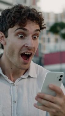 Şaşırmış Kafkasyalı iş adamı cep telefonuyla kazanan adam neşeli iş adamının internet üzerinden iyi haberler okuyarak kazanmasına şaşırdı. Şehirdeki internet zaferini kutlayın.