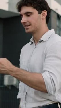 Şehirde yürüyen mutlu Kafkasyalı iş adamı cep telefonlu başarılı iş adamına bakıyor akıllı telefon yürüyüşü yapıyor ofis erkek işverenin yanına gidip online uygulamalara bakıyor.