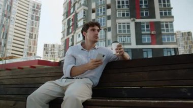 Kafkasyalı iş adamı içki içerek rahatlıyor cep telefonu uygulamasını kullanıyor gülümseyen akıllı telefon işadamı işçi adam çay içiyor kentteki sosyal medyada geziniyor.