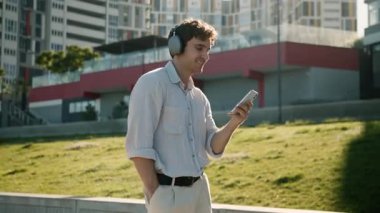 Aktif neşeli Kafkas iş adamı kulaklık takıyor cep telefonuyla müzik dinliyor şehir iş adamı erkek uzman dans uzmanı kulaklıkla müzik dinliyor akıllı telefon müzik uygulaması ile