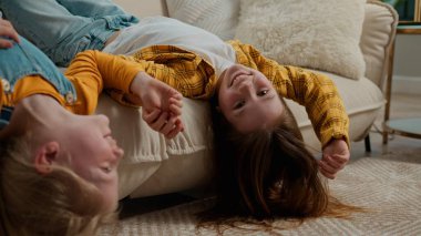 İki küçük neşeli Kafkasyalı kız çocuklar kız kardeşler kız kardeşler kız kardeşler kanepeye uzanmış el ele uzanmış kanepenin keyfini çıkarıyorlar gülüşmeler gülüşmeler ev arkadaşlığı sevincinde konuşmalar