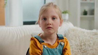 Ciddi ciddi sakin bir çocuk portresi. Kafkas çocuk kızı üzgün görünüyor. Evdeki kanepede poz veriyor.