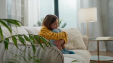 Hüsrana uğramış Kafkasyalı küçük kız kanepede dizlerini kucaklıyor çocuk çocuk evde tek başına acı çekiyor kötü ebeveyn velayet sorunu sağlık sorunu ergenlik çağındaki bebek koltukta kendini sıkıcı hissediyor.