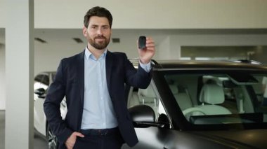 Otomobil galerisinde yeni araba anahtarlarını elinde tutan Kafkasyalı mutlu bir işadamı gülümseyen bir işadamı, gülümseyen bir erkek alıcı, araba satın alma şirketinin sahibi, anahtar sigorta salonu aracının ulaşımını gösteren bir bayilik kutluyor.