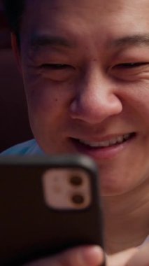 Yakın plan gülümseyen Asyalı 40 'lı yaşlardaki iş adamı cep telefonuna bak. Mutlu Koreli iş adamı Çinli uzman Japon ajan, gece ofisinde akıllı telefonla gülümsüyor.