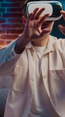 Asyalı orta yaşlı bir adam sanal gerçeklik kaskı kullanıyor. Gece kanepesinde VR oyunu oynuyor. Koreli Çinli erkek oyuncu Japon kullanıcı hava hologram arayüzünde metatif hareketler yapıyor.