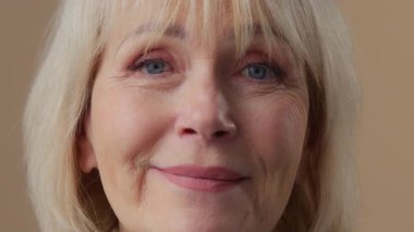 Beyaz, yaşlı, emekli kadın, emekli yaşlı kadın portre. Bej stüdyoda kameraya bakıyor. Gülümsüyor, mutlu, vesikalık, diş sağlığı için gülümsüyor.