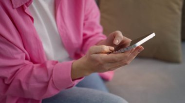 Tanımlanamayan beyaz bir kadın evinde oturuyor, cep telefonu yazıyor, sohbet ediyor, cep telefonu kullanıcısı, akıllı telefon uygulamasını tarıyor, sosyal medya internetinden alışveriş mesajları yazıyor.