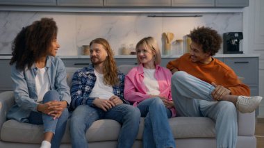 Çok ırklı, mutlu arkadaşlar kanepenin üzerinde sohbet ediyorlar. Kafkas erkekleri, Afrikalı kadınlar, iletişim kuran kızlar, içeride dostluk çeşitliliğinin tadını çıkarıyorlar.