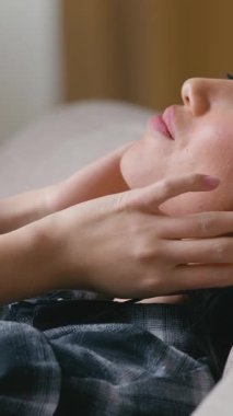 Sakin Asyalı genç bir kadın kulaklıkla müzik dinliyor. Kanepede gözleri kapalı. Rahat Koreli bir kadın kanepeye uzanıyor.