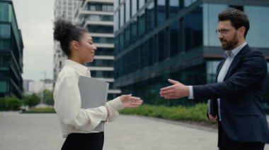 Kafkasyalı iş adamı Afrikalı iş kadınının elinde dizüstü bilgisayarla iş arkadaşlarıyla açık hava ortaklığı hakkında konuştuğu çok ırklı iş adamları tokalaşma toplantısı.