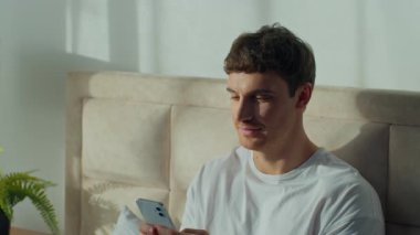 Beyaz adamın evde oturup cep telefonuyla Avrupalı bir erkeğe mesaj atması sohbet sohbetinin keyfini çıkarması mesajlar yazması akıllı telefonlara bakması dinlendirici yatak odasında dinlendirici rahatlama.