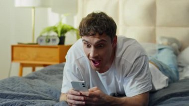 Mutlu Kafkasyalı adam evinde uzanmış elinde akıllı telefonuyla zafere seviniyor. İyi haber mesajı okuyan neşeli erkek arkadaşın mutluluğu zaferin tadını çıkarıyor.