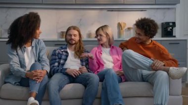 Çok ırklı, mutlu arkadaşlar kanepenin üzerinde sohbet ediyorlar. Kafkas erkekleri, Afrikalı kadınlar, iletişim kuran kızlar, içeride dostluk çeşitliliğinin tadını çıkarıyorlar.