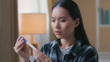 Şaşırmış, endişeli, hamile, test sonuçlarını bekleyen Asyalı bir kadın. Evde oturan, endişeli, mutsuz, Koreli bir kız. Beklenmedik bebek sorunu.