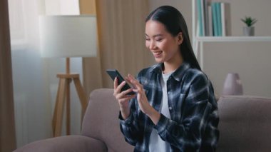 Kharkiv, Ukrayna - 24.12.2021: Evde akıllı telefon kullanan gülümseyen Asyalı kadın, internet üzerinden sohbet eden, teslimat servisi alışverişi yapan, internet üzerinden alışveriş yapan, indirimli cep telefonu.