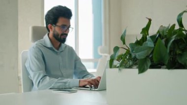 Gülümseyen Arap Hintli iş adamı, ofis içinde dizüstü bilgisayarda çalışıyor, e-posta yazıyor, bilgisayar direktörü erkek işadamı yönetici girişimci online sohbet, internet üzerinden iş yeri programlama.